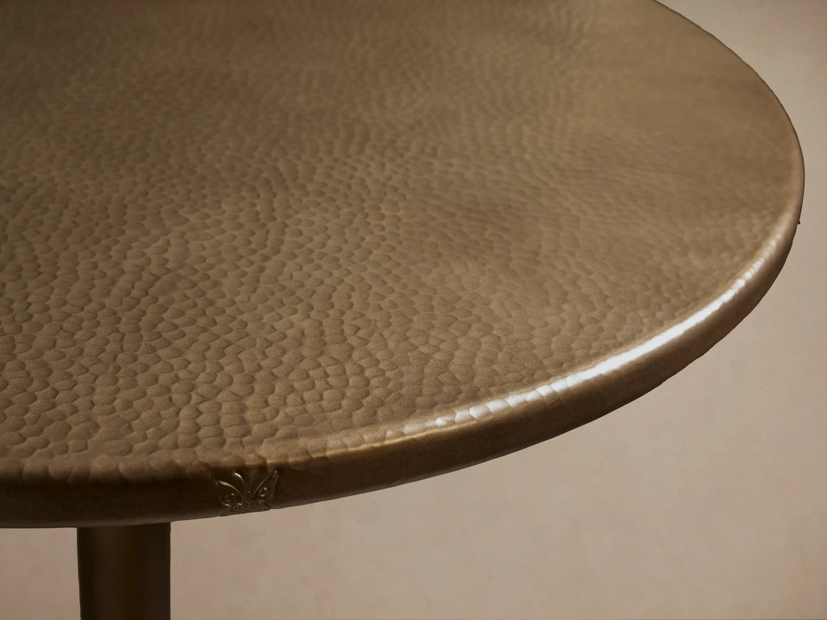 Recycled Metal Bar Table with a round bronze-colored top and a matching Wade base, standing on a wooden floor.