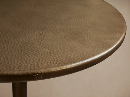 Recycled Metal Bar Table with a round bronze-colored top and a matching Wade base, standing on a wooden floor.