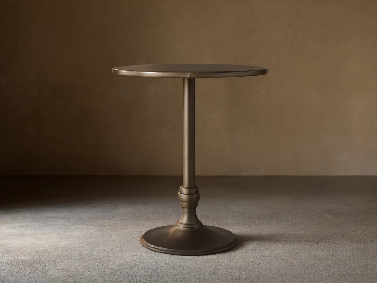 Recycled Metal Bar Table with a round bronze-colored top and a matching Wade base, standing on a wooden floor.