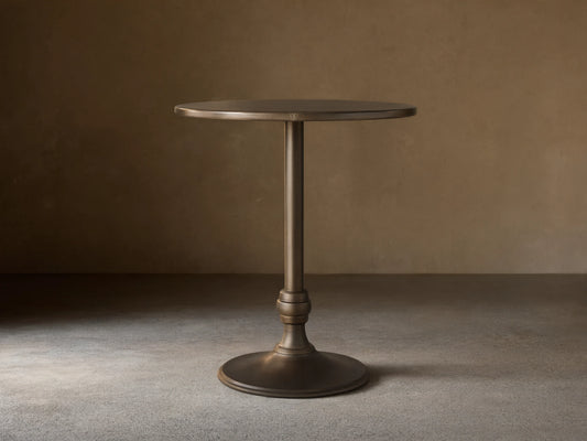 Recycled Metal Bar Table with a round bronze-colored top and a matching Wade base, standing on a wooden floor.