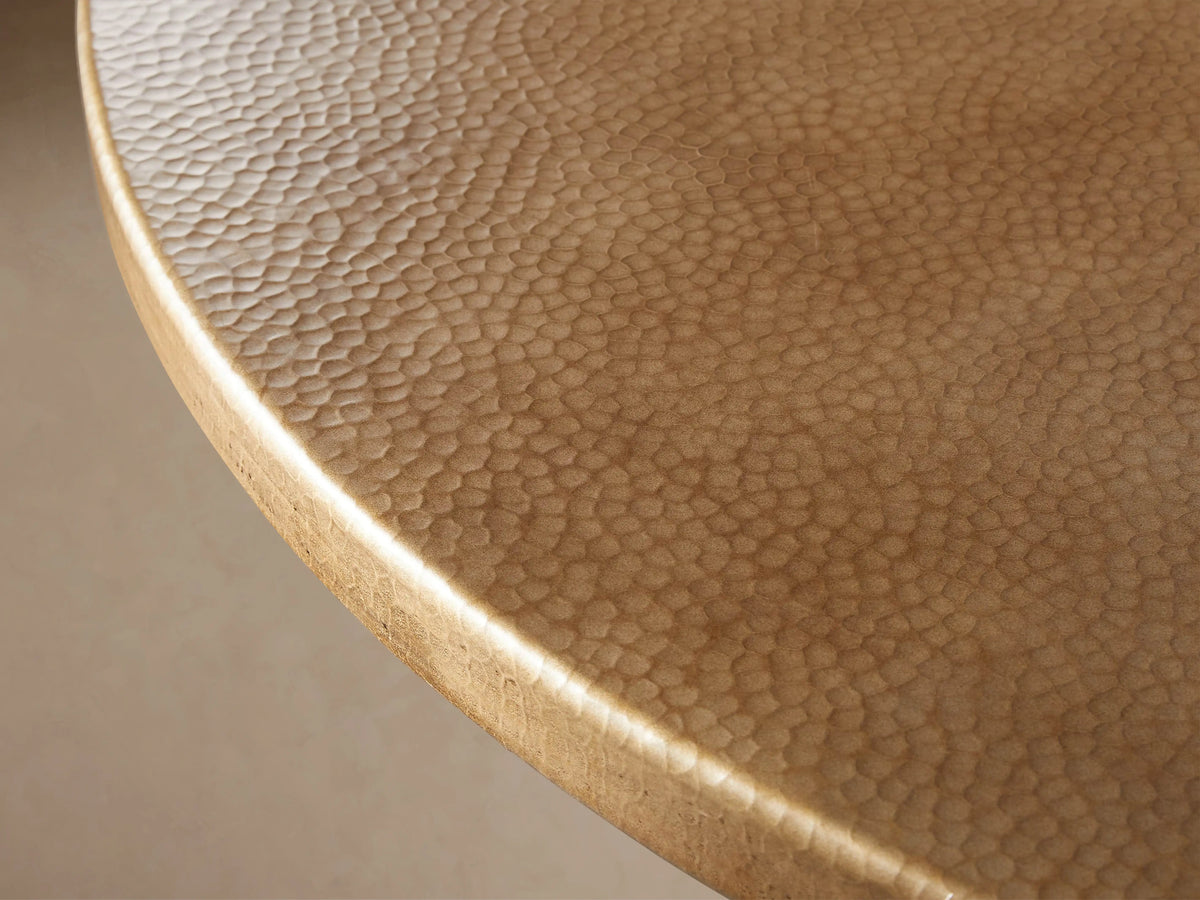 Round brass-finished recycled metal bistro tabletop, hammered texture, viewed from above on a light beige background.
