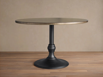 Recycled Metal Dining Table with Wade Base. Round bronze metal top, black ornate pedestal base on wooden floor.