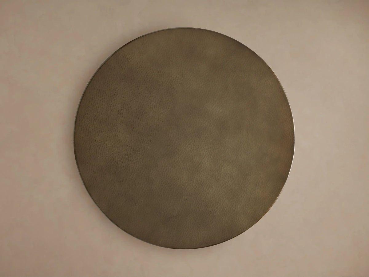 Close-up of a Recycled Metal Dining Table. Round, golden, hammered tabletop with a reflective edge on a black Wade base.