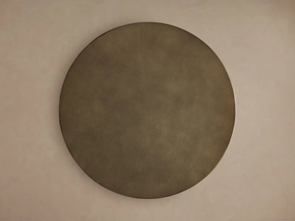 Close-up of a Recycled Metal Dining Table. Round, golden, hammered tabletop with a reflective edge on a black Wade base.