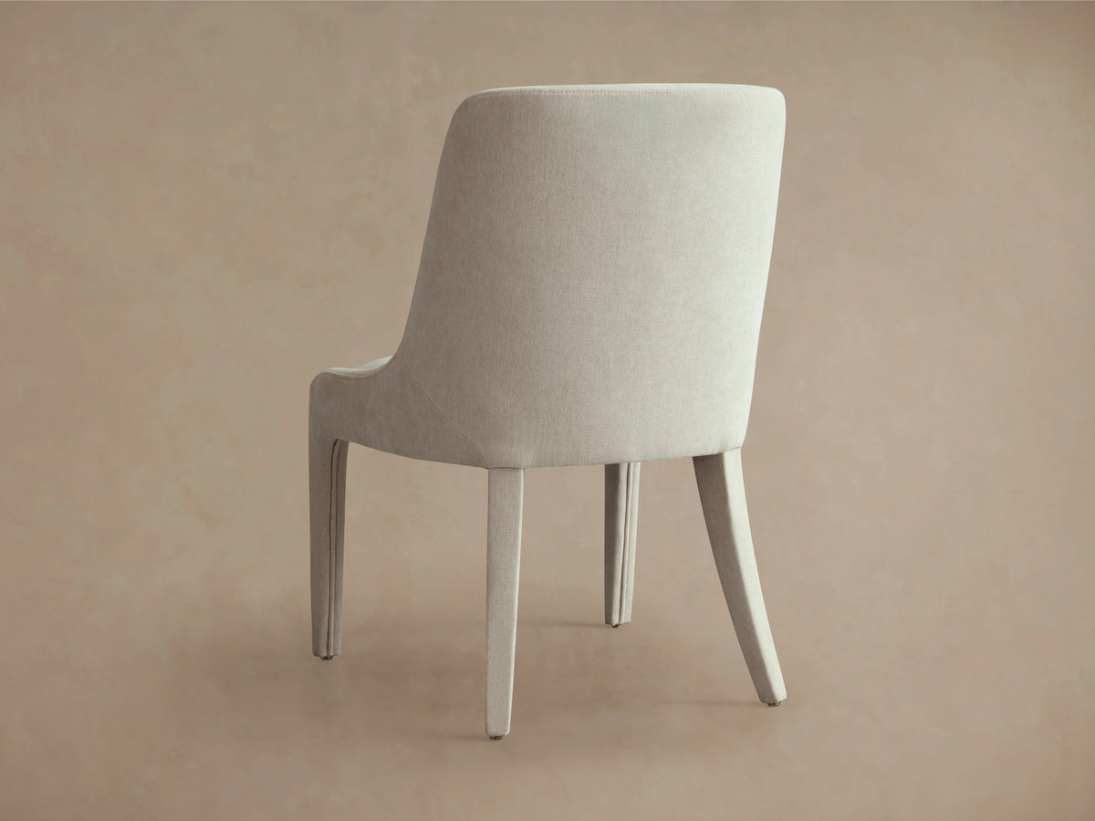 Burns Dining Chair in beige with elegant, fully upholstered frame, rounded backrest, and dense foam seat on a wooden floor.