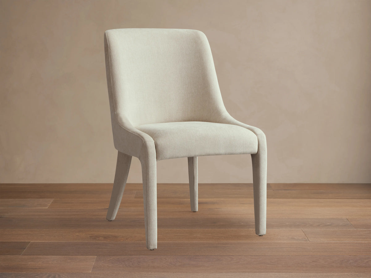 A rear view of the Burns Dining Chair, fully upholstered in a light fabric, featuring elegantly rounded backrest and sturdy legs.