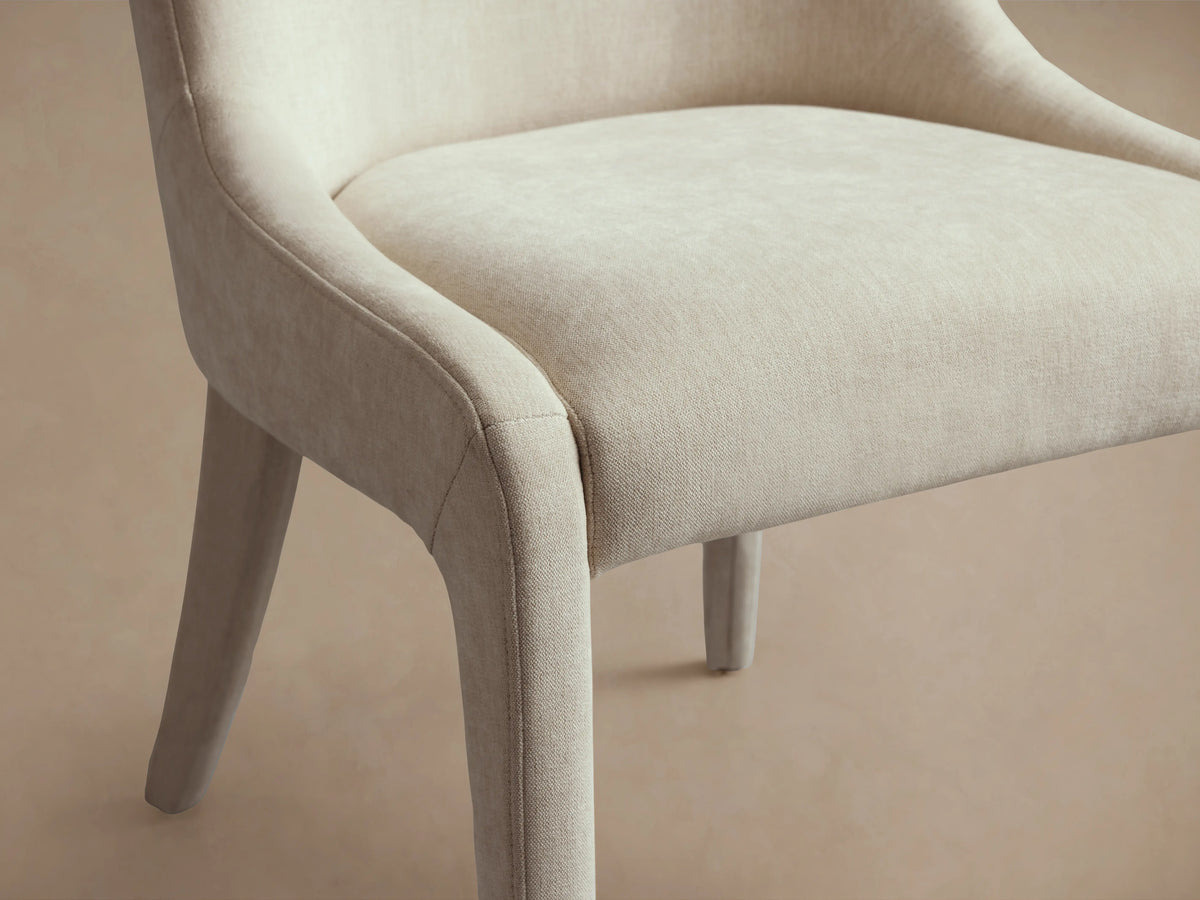 Burns Dining Chair with beige upholstery, featuring a fully cushioned seat and rounded backrest. Positioned on a wooden floor.