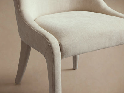 Burns Dining Chair in light beige upholstery with rounded backrest and smooth seat on wooden floor, viewed from the front.