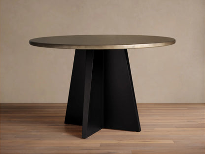 Recycled Metal Round Dining Table with a warm brassy top and a flat black vertex base, standing on a wooden floor.