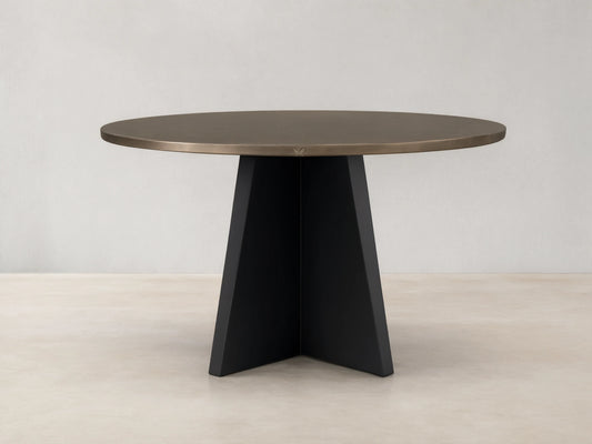 Round recycled brass-toned metal dining table with a sharp black iron Vertex Base, centered on a light wood floor.