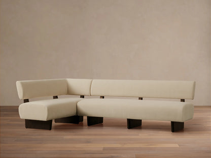 L-shaped Beau Banquette in cream fabric, featuring a sleek, minimalist design with dark wood exposed frame & legs, on wood floor.