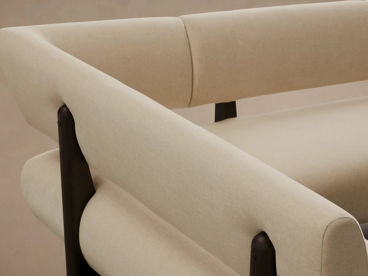 L-shaped Beau Banquette, cream upholstered sectional with a dark exposed wood frame and legs, on a wooden floor.