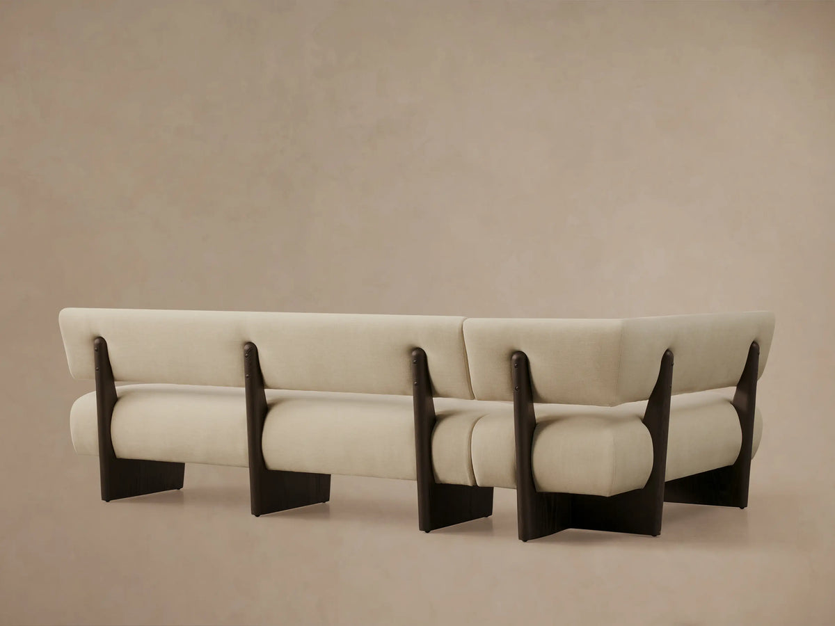 Angled close-up of Beau Banquette: light beige upholstered seat and backrest cushions with dark wood exposed frame.