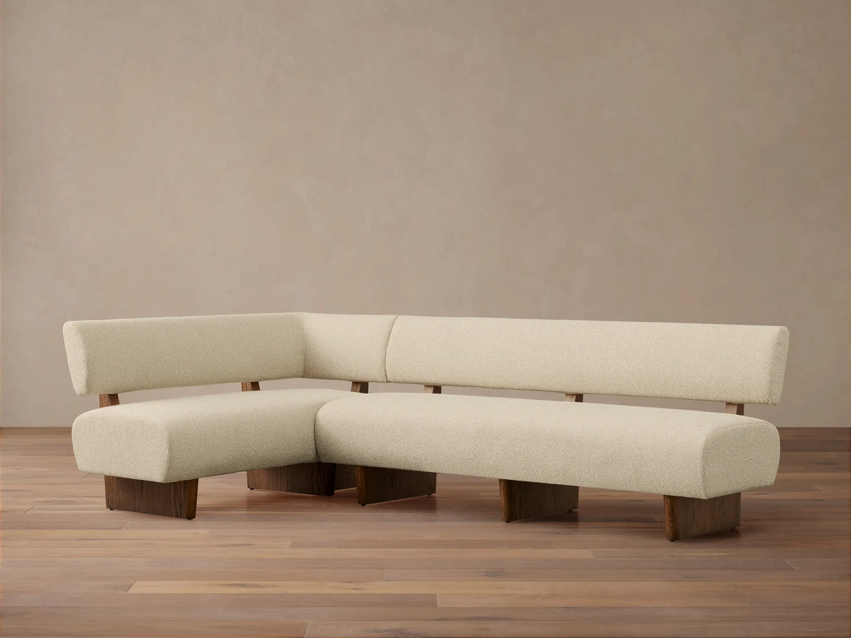 Beau Banquette: L-shaped cream bouclv© sofa with dark wood frame, legs, and back supports, on a wooden floor.