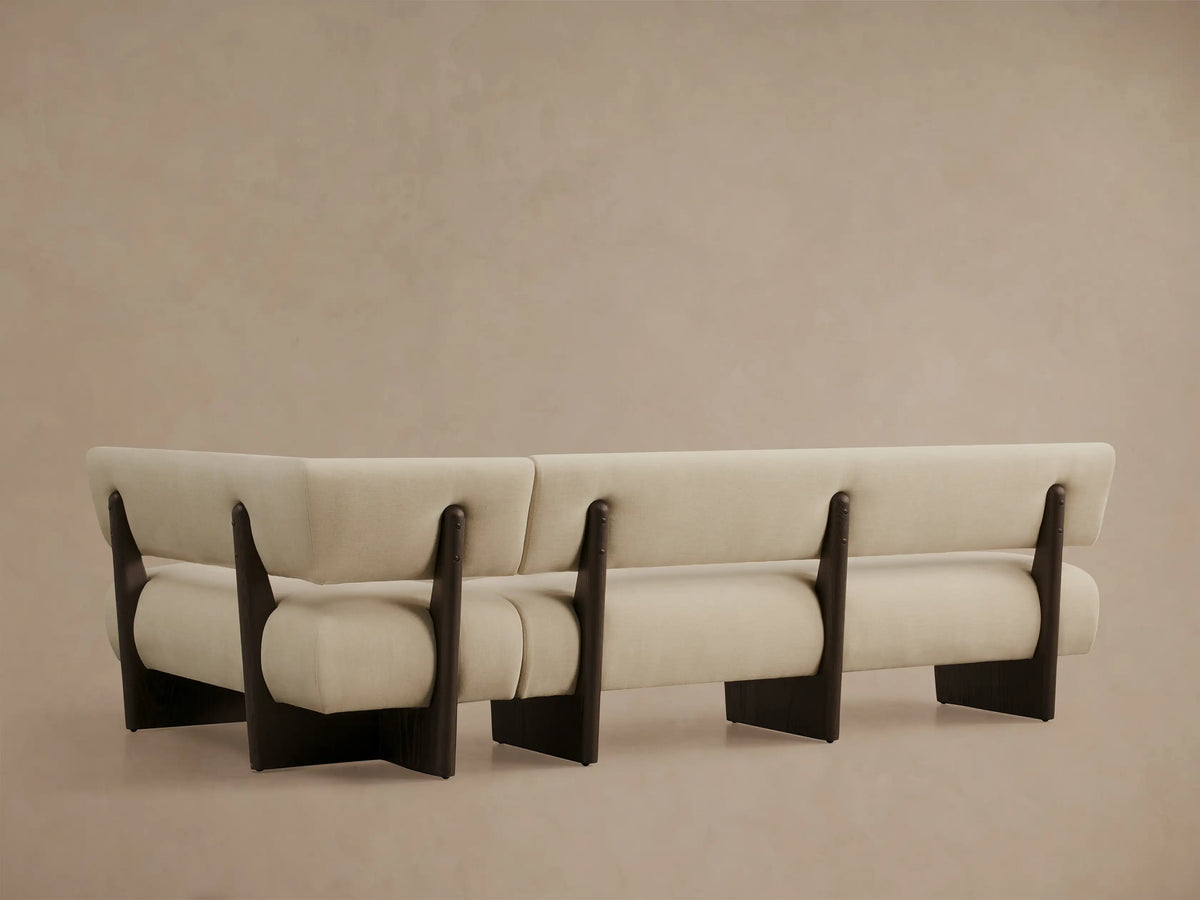 Close-up of a cream Beau Banquette, angled view showing its curved back and armrest with dark wood frame details.