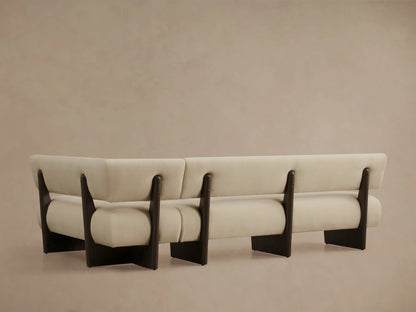 Close-up of a cream Beau Banquette, angled view showing its curved back and armrest with dark wood frame details.