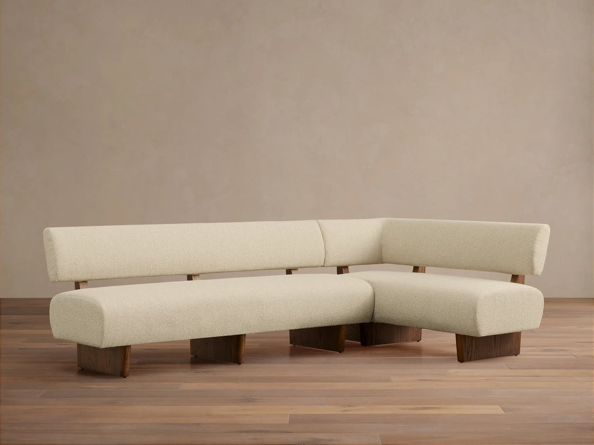 Beau Banquette, L-shaped, cream textured upholstery on a dark wood frame, angled on a wood floor against a light wall.