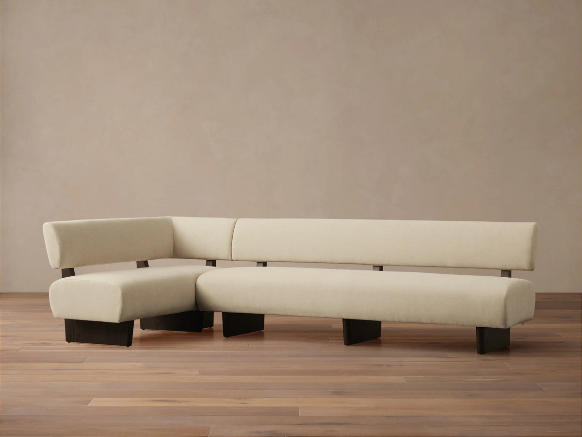 Beau Banquette, L-shaped sofa in cream upholstery with exposed dark wood frame, against a light tan wall on a wooden floor.