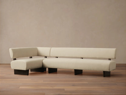 Beau Banquette, L-shaped sofa in cream upholstery with exposed dark wood frame, against a light tan wall on a wooden floor.