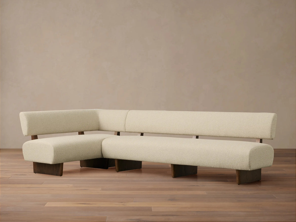 Beau Banquette: L-shaped cream bouclv© banquette with dark wood exposed frame and legs, on a wood floor against a light wall.