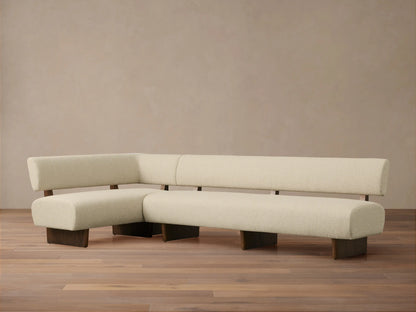 Beau Banquette: L-shaped cream bouclv© banquette with dark wood exposed frame and legs, on a wood floor against a light wall.