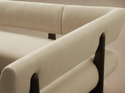 L-shaped Beau Banquette with cream fabric upholstery & dark exposed wood frame, on a wood floor against a plain wall.