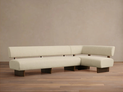 L-shaped Beau Banquette in cream textured upholstery with exposed dark wood frame and legs, on a wooden floor.