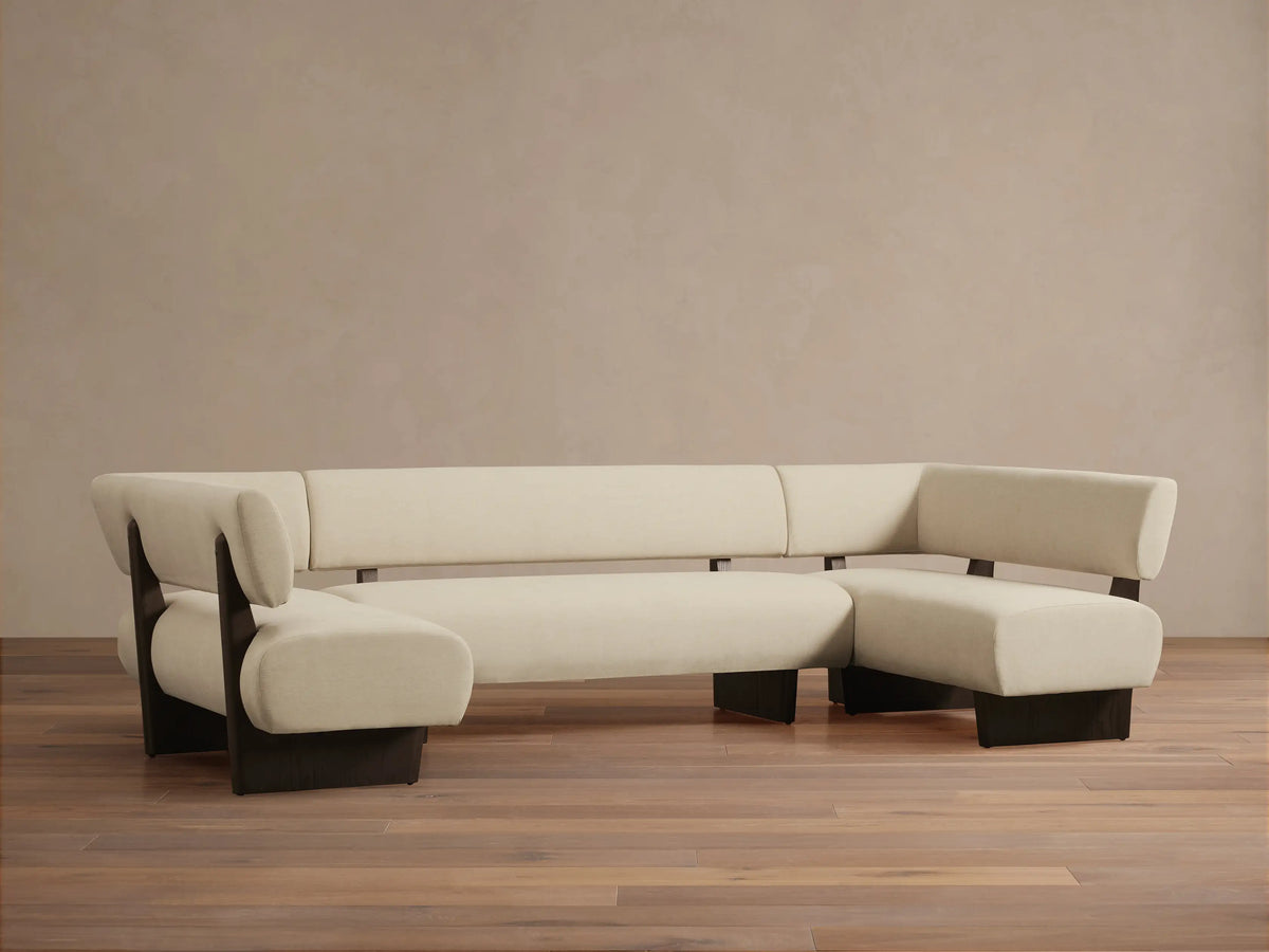 Cream Beau U-shaped banquette with dark exposed frames, modular sections, and curved ends, front view on a wooden floor.