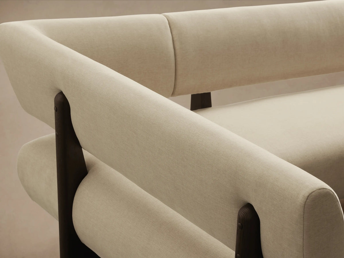 L-shaped cream Beau Banquette with dark exposed wood frame, against a plain wall on a hardwood floor.