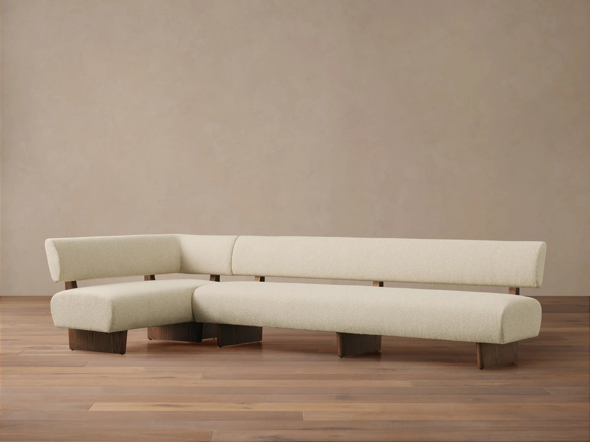 Beau L-shaped Banquette with cream bouclv© upholstery and a dark exposed wood frame.