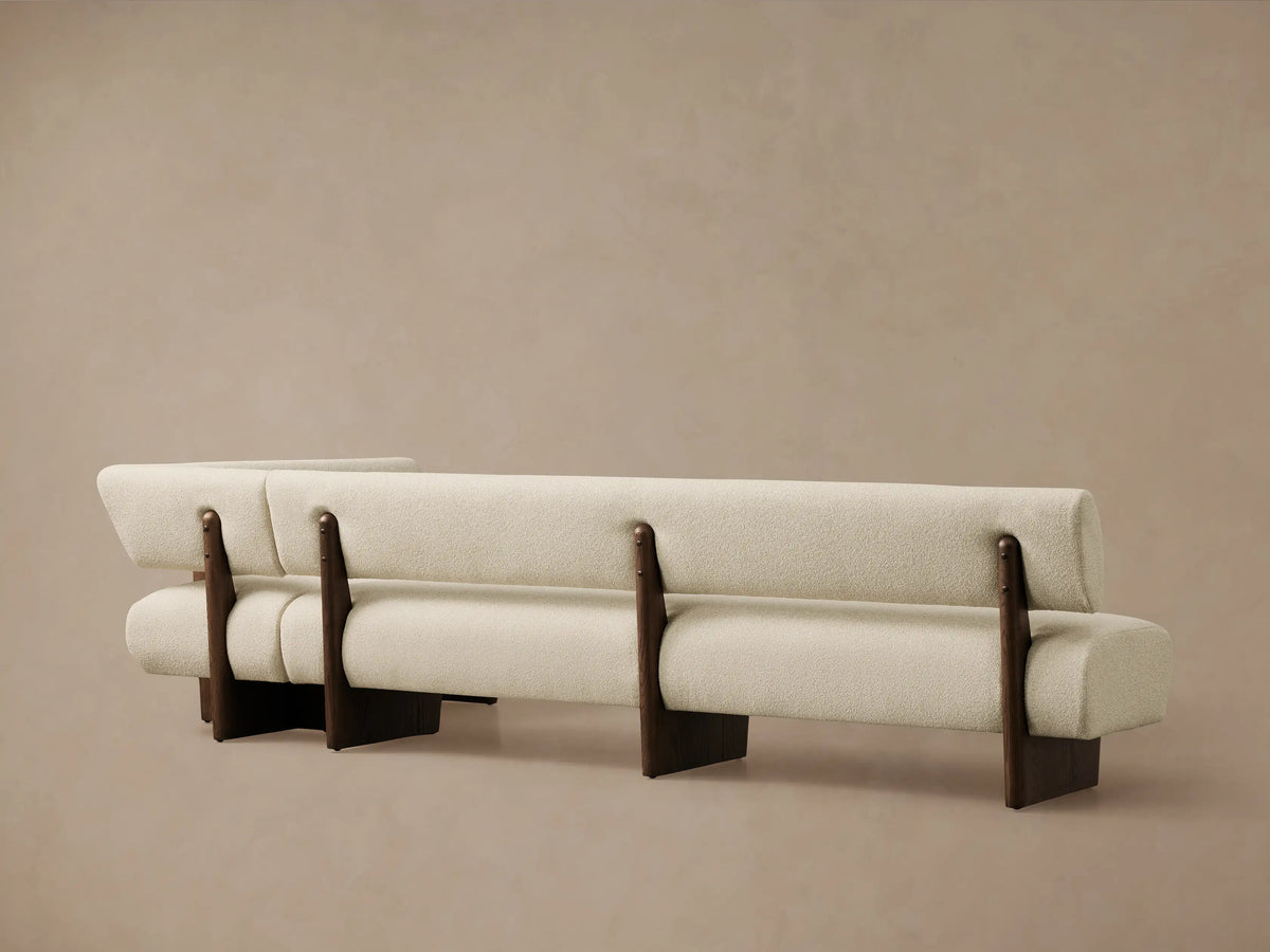 Beau Banquette, a creamy, textured fabric corner bench with dark oak veneer frame and exposed wood details.