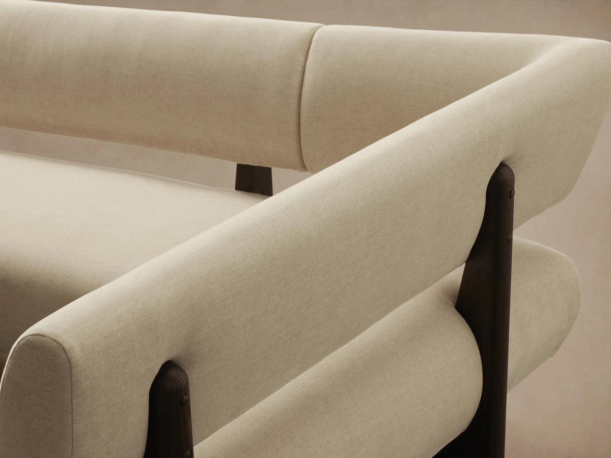 Beau Banquette, L-shaped, light cream upholstered, dark wood frame & legs, on a wood floor.