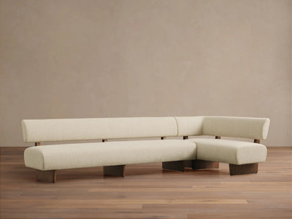 Beau Banquette, an L-shaped sofa with cream textured upholstery, dark wood base & exposed supports, on a wood floor.
