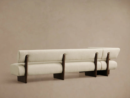 Light beige bouclv© Beau Banquette with a dark wood exposed frame, viewed from an angle showing its curved back and seat cushions.