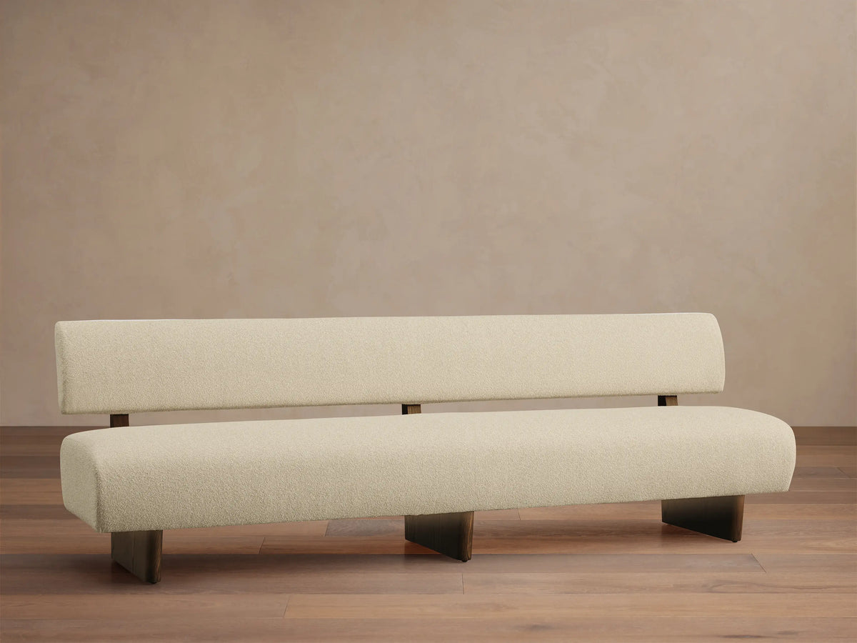 Beau Banquette, cream boucl?? fabric, minimalist design with separated backrest, dark wood legs on a wooden floor.