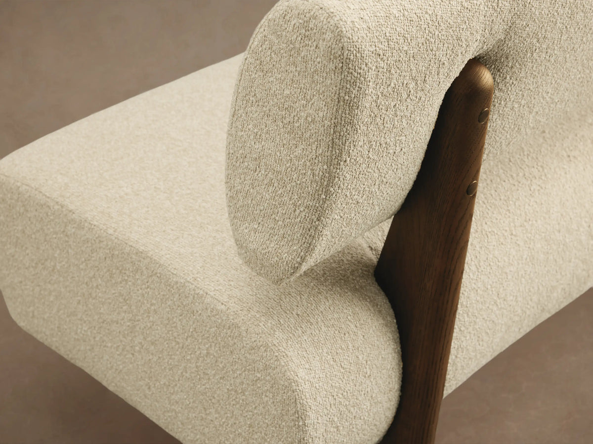 Cream boucle Beau Banquette with a floating backrest & curved seat, supported by dark angled legs on a wood floor.