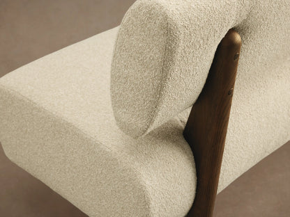 Cream boucle Beau Banquette with a floating backrest & curved seat, supported by dark angled legs on a wood floor.