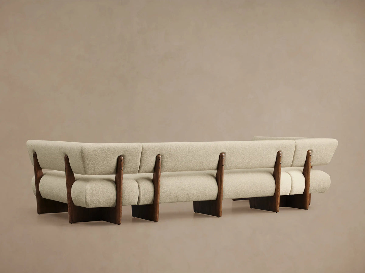 Angled close-up of Beau U-Shaped Banquette. Light cream textured upholstery on curved arm and back, with dark wood frame.