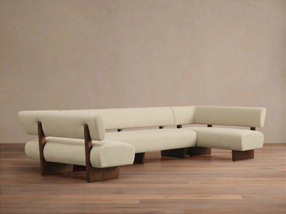 Cream bouclv© Beau U-Shaped Banquette with dark wood frame and legs on a wooden floor, against a light beige wall.