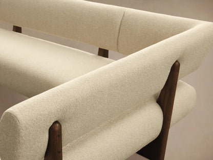 Beau U-shaped banquette with cream bouclv© upholstery and dark wood frame, on a light wooden floor.