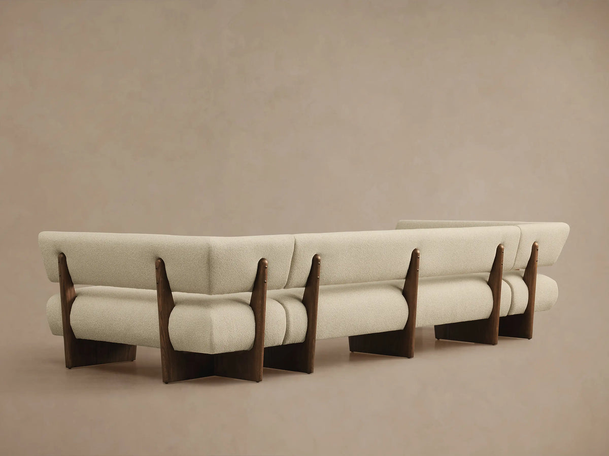 Angled view of a Beau U-Shaped Banquette, featuring light cream textured fabric upholstery and dark wood supports.