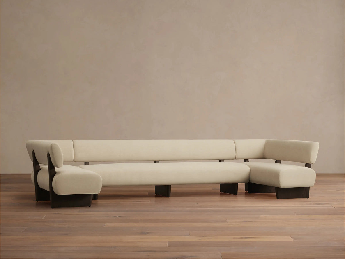 Beau U-Shaped Banquette, cream upholstery with dark wood frame, on a wooden floor against a light beige wall.