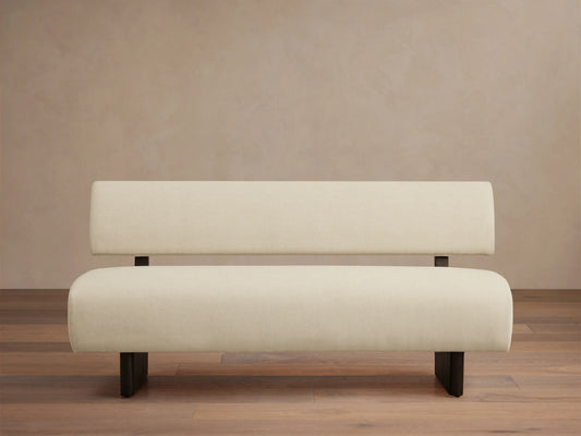 Beau Banquette: Off-white upholstered bench with a distinct backrest and dark, minimalist legs, on a wooden floor.