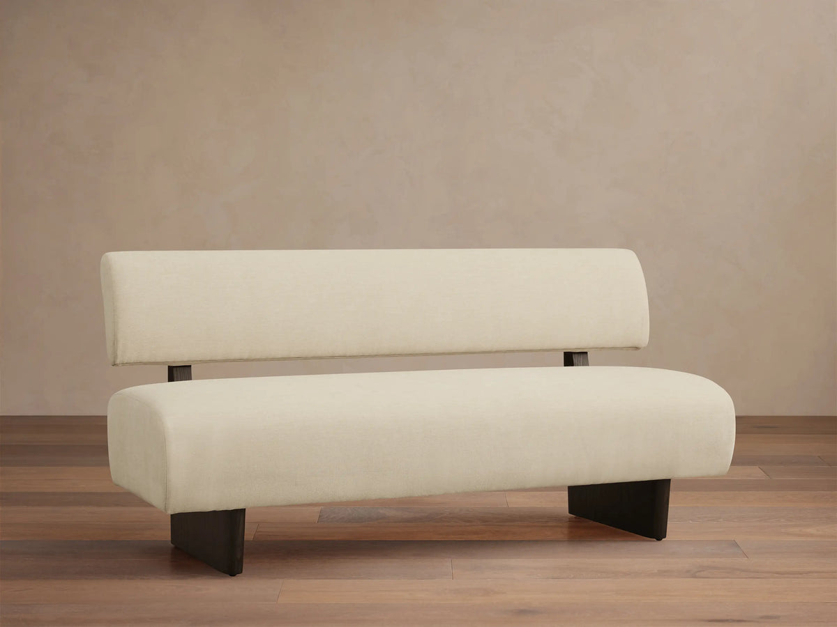 Beau Banquette: Off-white upholstered bench with a distinct backrest and dark, minimalist legs, on a wooden floor.