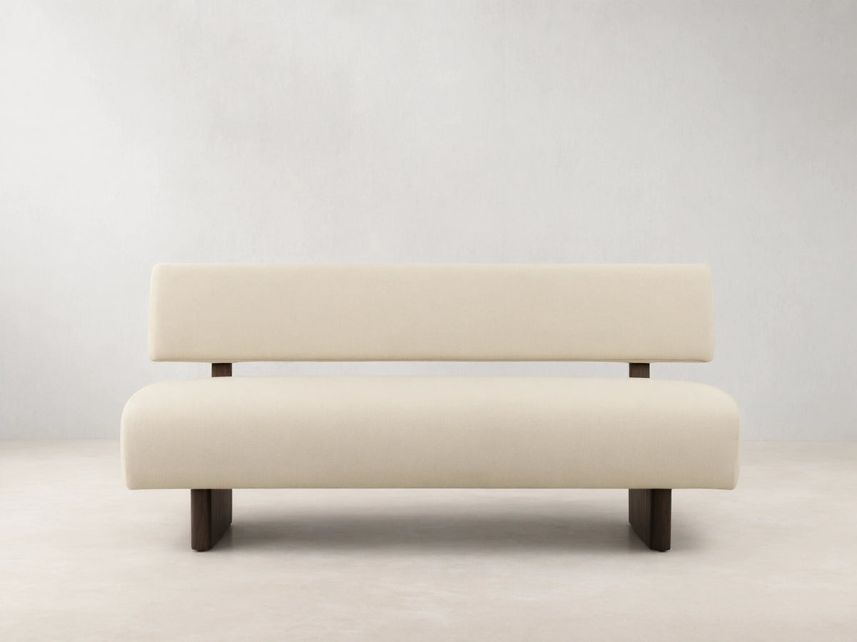 Beau Banquette: Off-white upholstered bench with a distinct backrest and dark, minimalist legs, on a wooden floor.