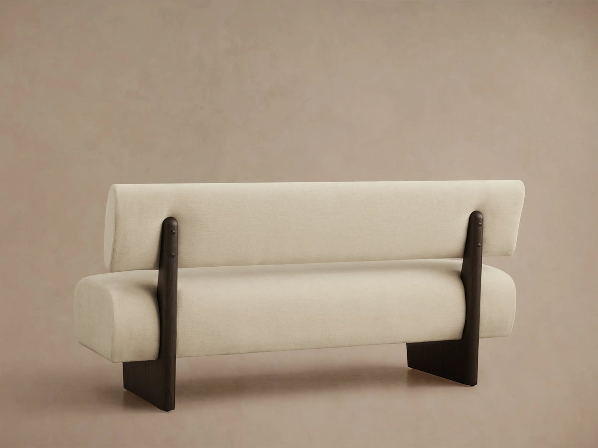 Close-up of Beau Banquette, showing its cream fabric upholstery and a dark brown wooden armrest from a top-down angle.