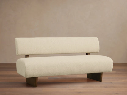 Beau Banquette: creamy white boucl?? fabric with dark wooden legs & suspended backrest, centered on a wood floor.