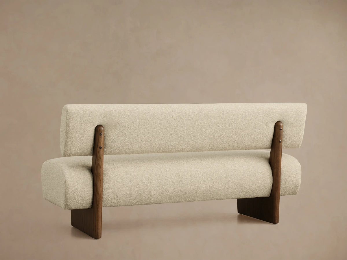 High-angle view of a Beau Banquette upholstered in light beige textured fabric with a dark wooden frame and curved backrest.