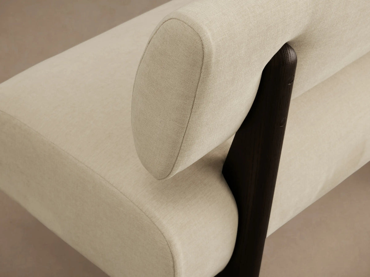 Light cream upholstered Beau Banquette with a curved seat, straight backrest, and dark wooden block legs on a wooden floor.