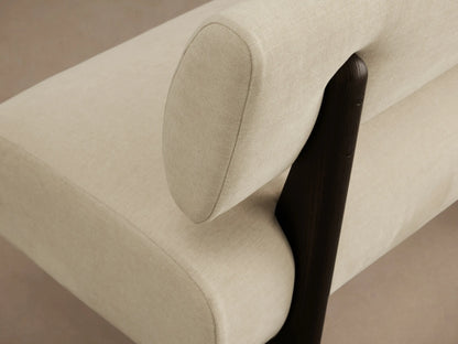 Light cream upholstered Beau Banquette with a curved seat, straight backrest, and dark wooden block legs on a wooden floor.